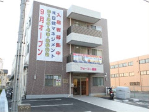 目の前に駐車場とタイル張りのアプローチを有した施設の外観