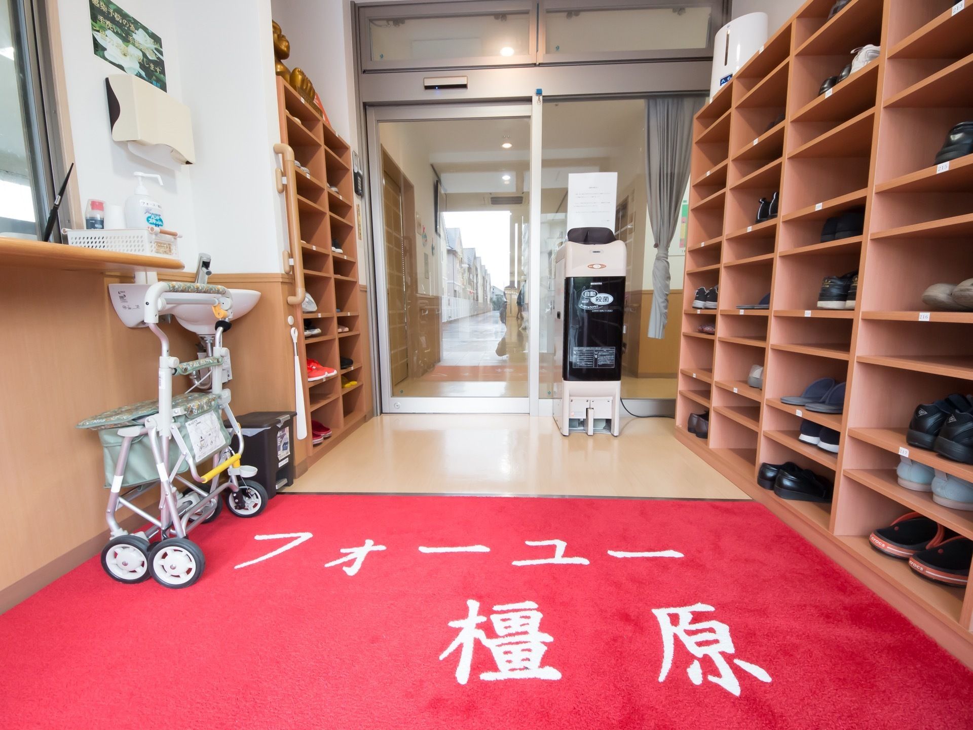 玄関には、施設名称が入った赤い泥落としマットが敷かれている。両サイドには、靴箱や受付カウンター、手洗い場が設置されている。