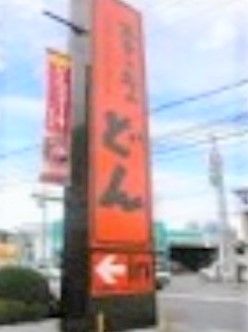 オレンジ色を背景に、黒文字で店舗名が書かれた看板である。ステーキなどの肉料理を中心としたレストランで、施設近くに立地している。