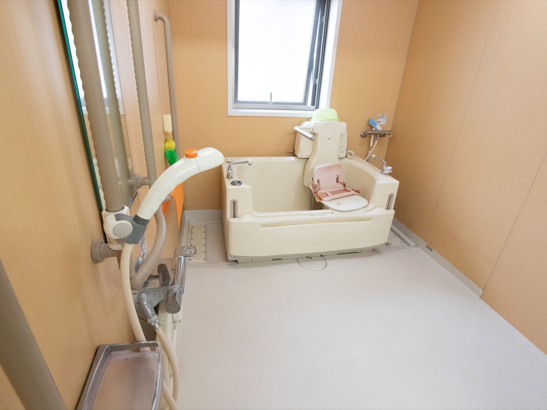 浴室は窓が設置され、介護用の入浴装置が窓際に設置されている。壁には、縦型の手すりが取りつけられている。手前にはシャワーもついている。