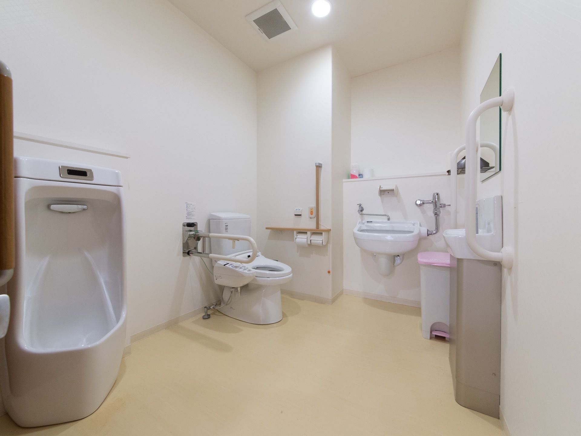 洋式便器、男性用便器、オストメイト対応型便器を備えた広いトイレである。ナースコールや洗面台も備わっている。