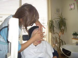 顔をやさしくマッサージしている女性エステシャン。高齢女性は座って肩回りにタオルをかけている。