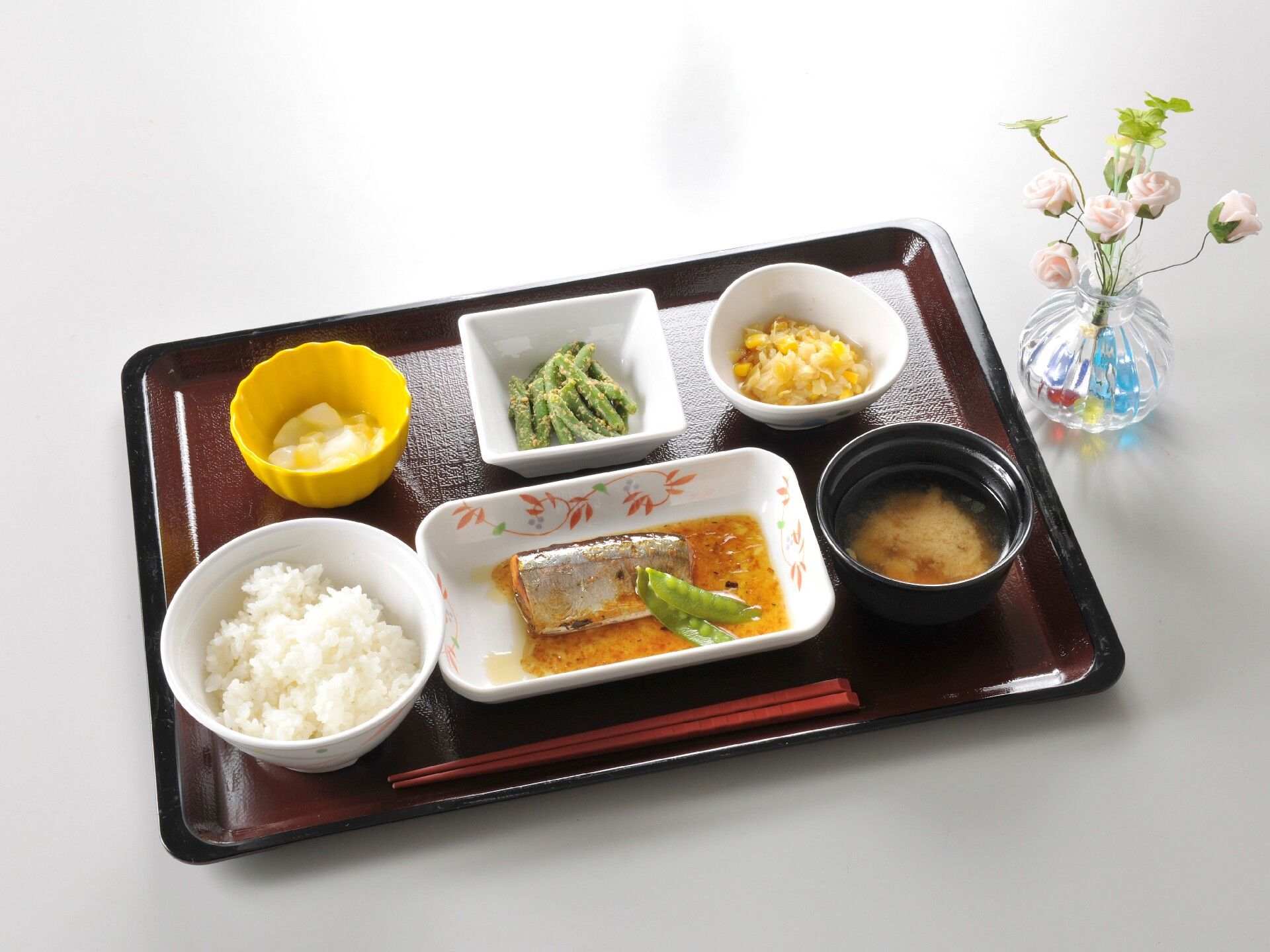 魚料理や白いご飯に味噌汁、いんげんの胡麻和えなどが並べられたトレーの横には花も飾られている。