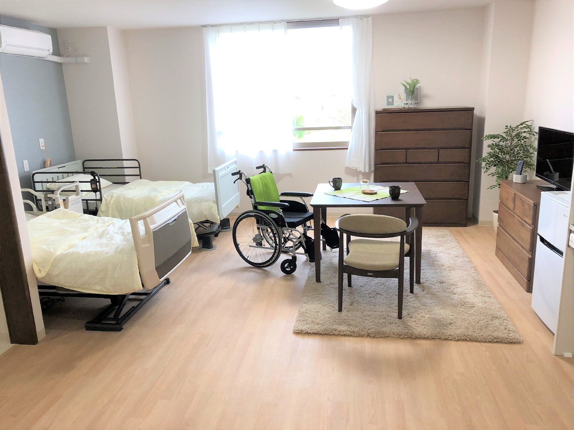 タンスやテーブルセット、寝具付きのベッドが2台置かれたフローリングの部屋には大きな窓が付いている。
