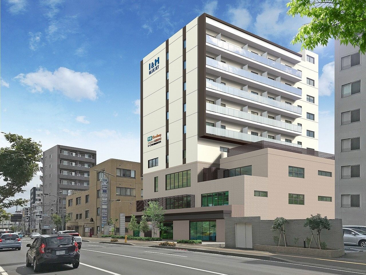 道路に面した場所に建っている白とベージュの9階建ての建物。周りにもたくさんの建物がある。