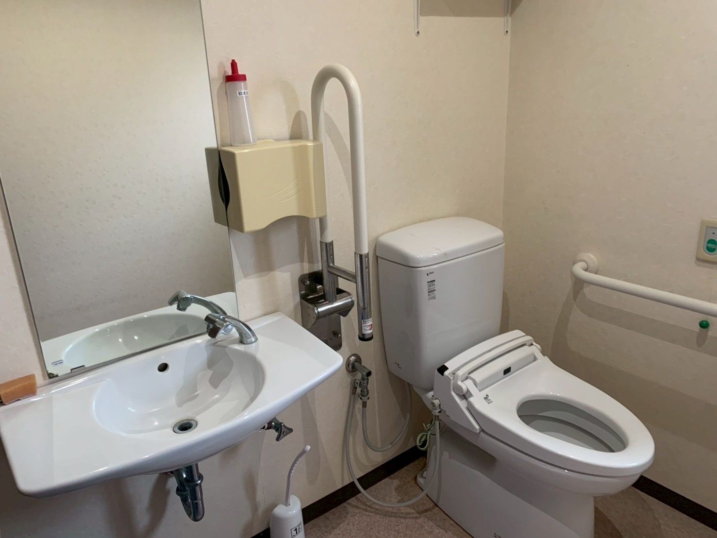 ニット帽をかぶった車いすの高齢女性に付き添い、屋外で笑顔で過ごしているエプロンを付けた女性スタッフ。