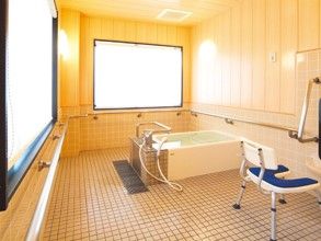 広い床と大きな窓、シャワーチェアーや手すり、浴槽が設置されている浴室