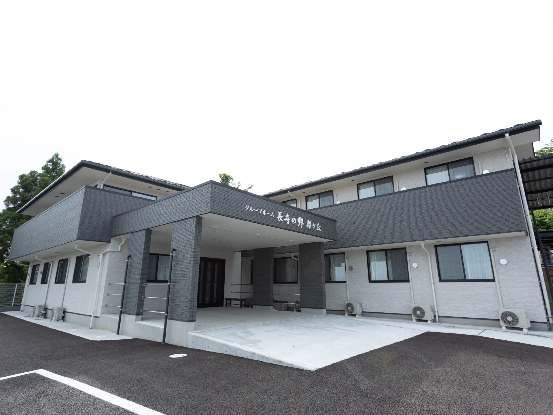 車いすの高齢女性が笑顔でそばにいるエプロンを付けた若い女性スタッフと手を取り合っている。