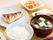 白いご飯に味噌汁、焼き魚、漬物、野菜の和え物などが並び、箸が添えられている。