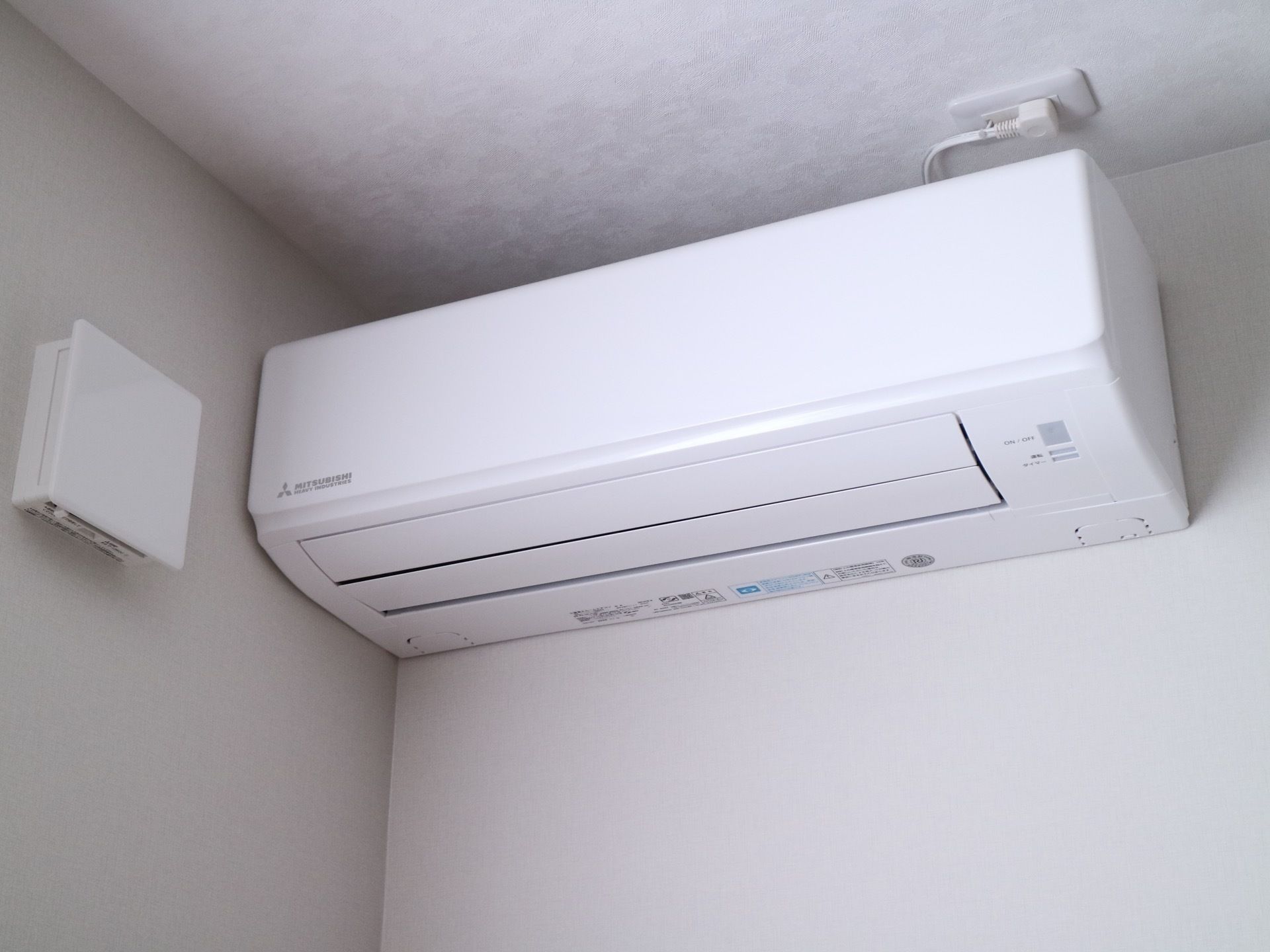 シンプルな白いエアコンが設置された白い壁。エアコンのそばには空気の換気システムもある。