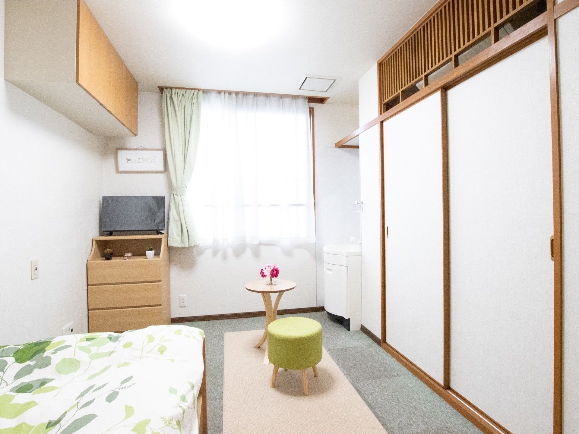 天井からの釣り戸棚があり、その下にはテレビが置かれている。また、部屋の奥には白い洗面台が設置されている。