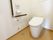 エル字型の手すりが設置されたトイレにはオレンジの呼び出しボタンもあり、トイレットペーパーホルダーもある。