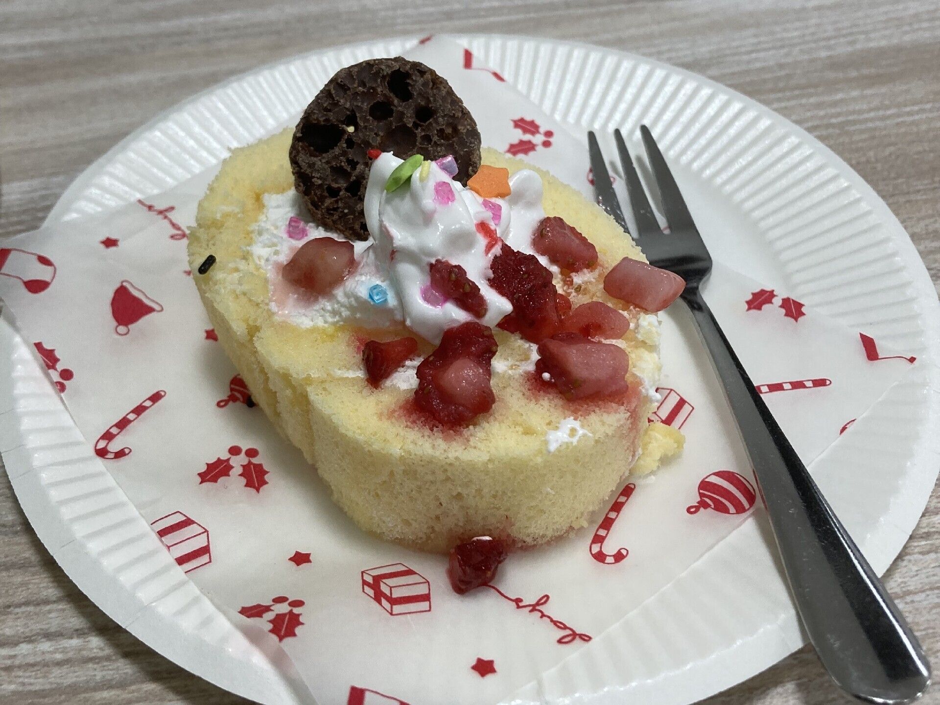 クリームやフルーツなどがトッピングされたロールケーキが一切れ、紙皿に盛られている。
