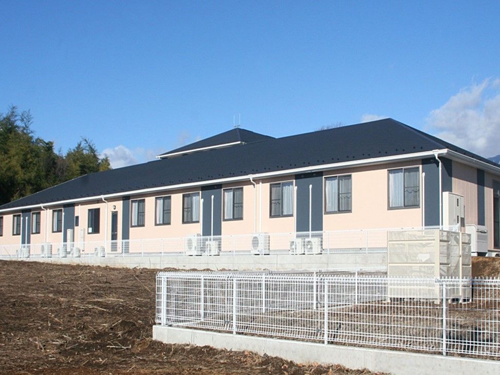 周りに草地があるベージュ色の外壁で三角屋根の平屋建築物