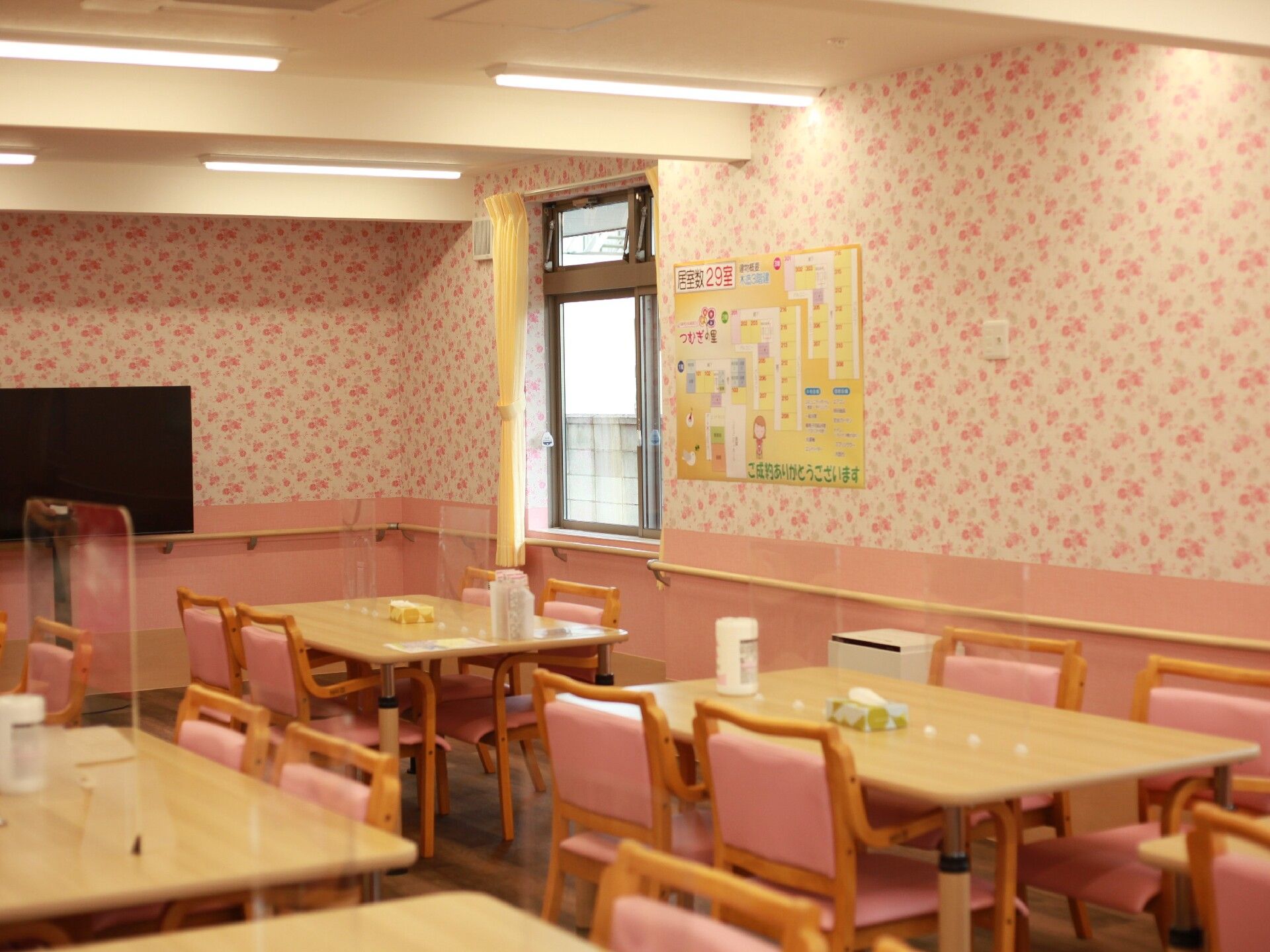 車いすの高齢女性と付き添いの高齢男性。両サイドには若い男女のスタッフがいて、屋外で笑顔で過ごしている。