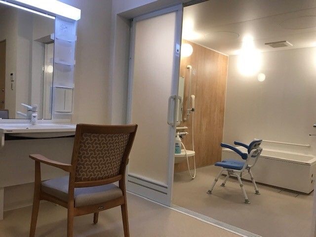 シャワーチェアが置いてある浴室と、手前に椅子が置いてある洗面台の写真