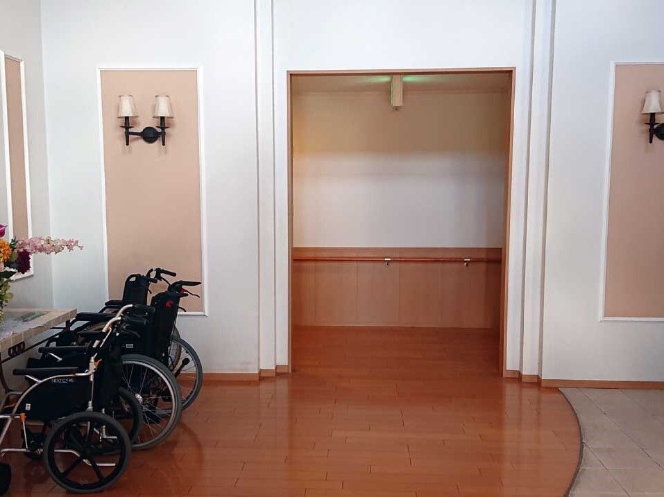 車いすが数台置かれたホールには花が飾られている。段差はなく、壁には手すりが付いている。