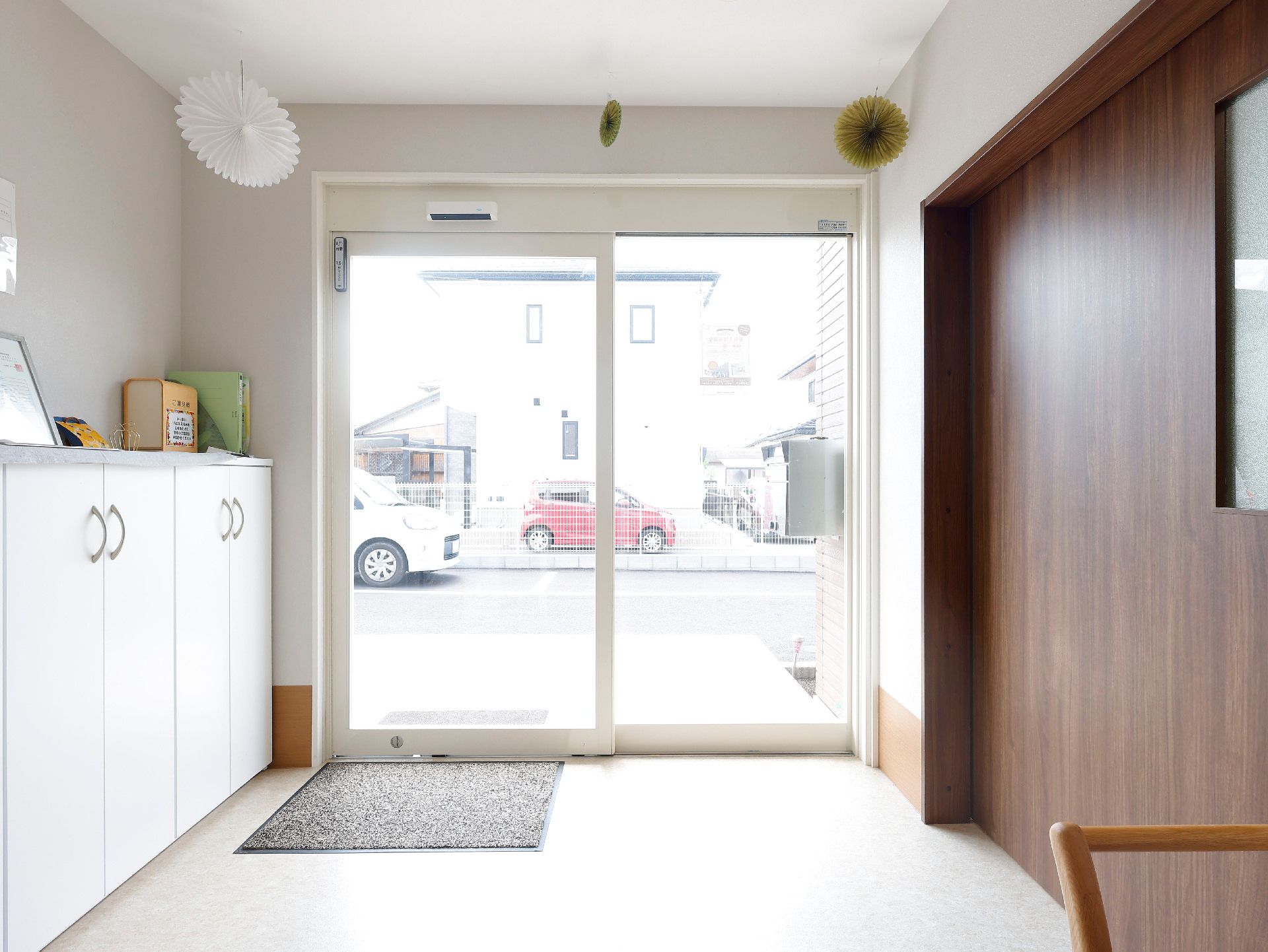 白い棚と茶色い扉に挟まれた自動ドアがある建物の入り口