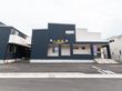 モノトーンの外壁の２階建ての建物。ホーム名が外壁に書かれ、玄関には手すり付きの階段とスロープがある。