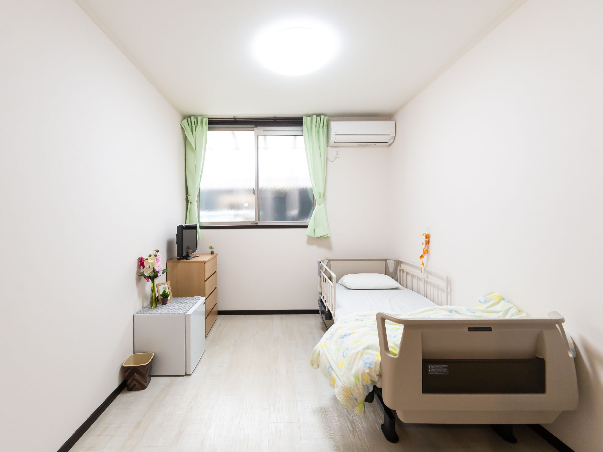 大きな窓にはカーテンが付き、壁にはエアコンがあり、フロアには寝具付きのベッドがある。