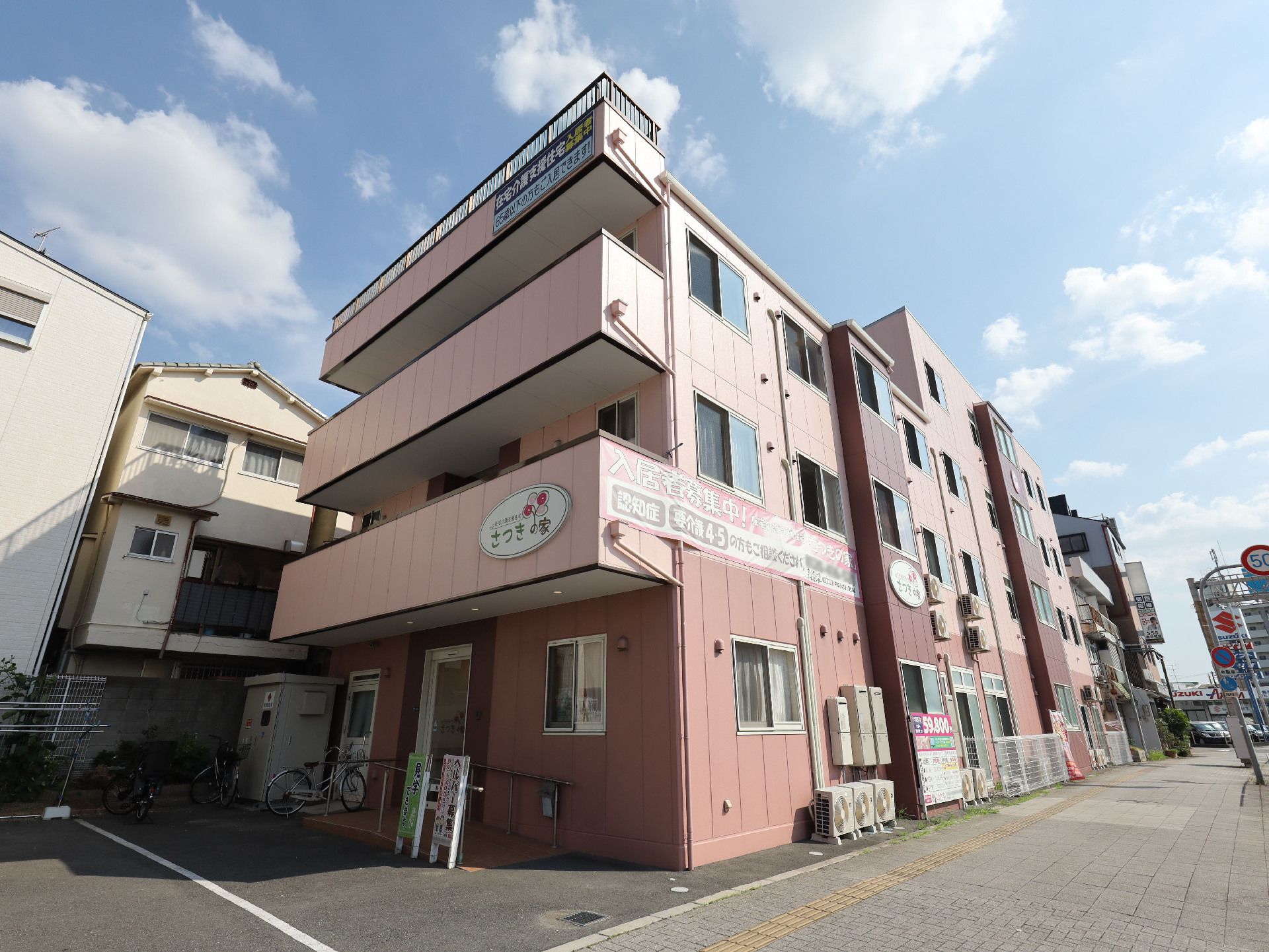 歩道沿いに立地しているピンクの外観のベランダが付いた３階建ての建物