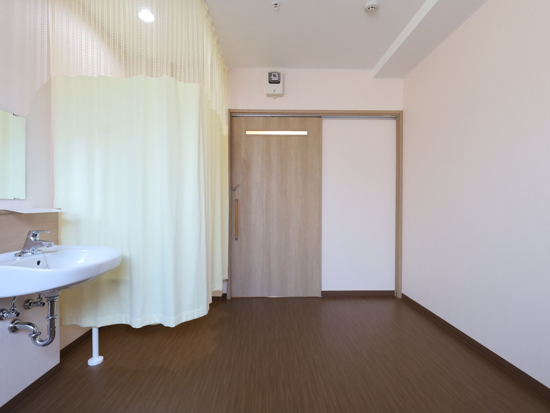 一角がカーテンで仕切られた洗面台とスライド式の扉がある白い壁の部屋