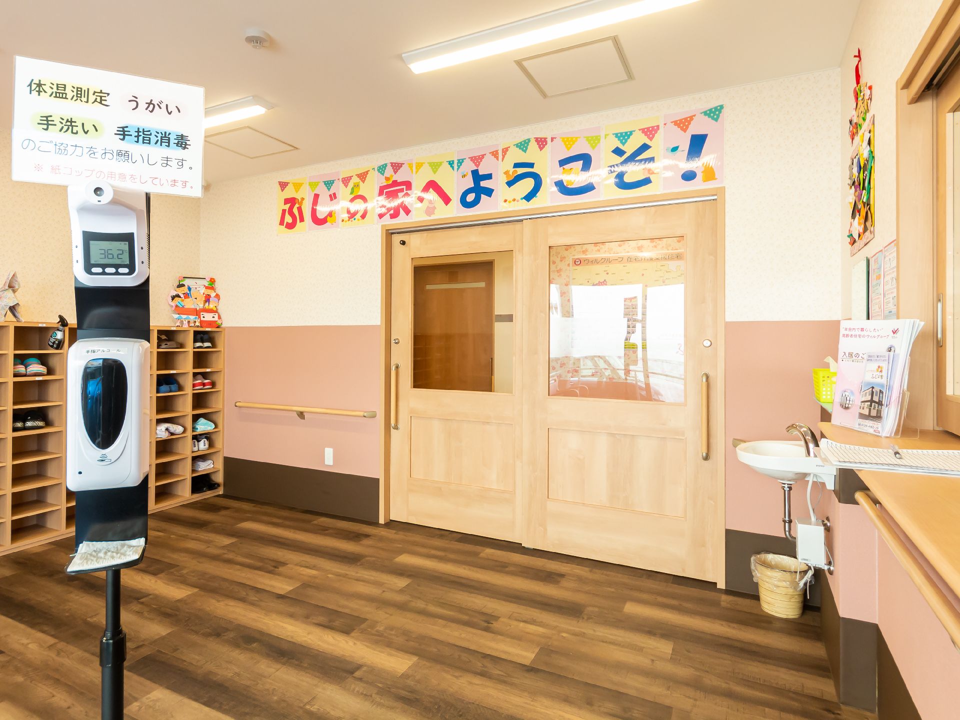 靴箱と受付口に挟まれたアルコール消毒が置かれた建物のエントランス