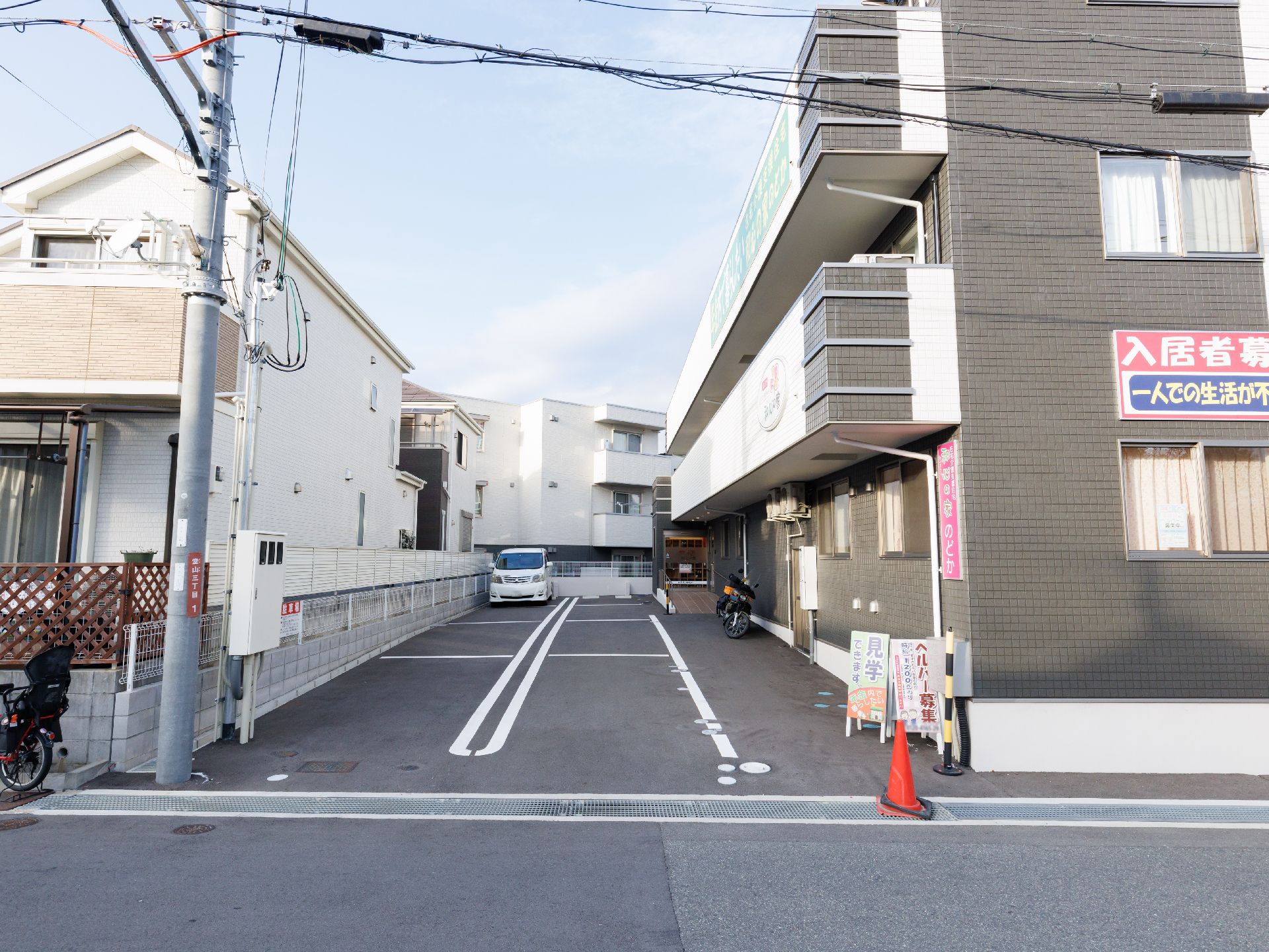 ３階建ての建物は各フロアにベランダがあり、敷地内には駐車場もあり、車が止まっている。