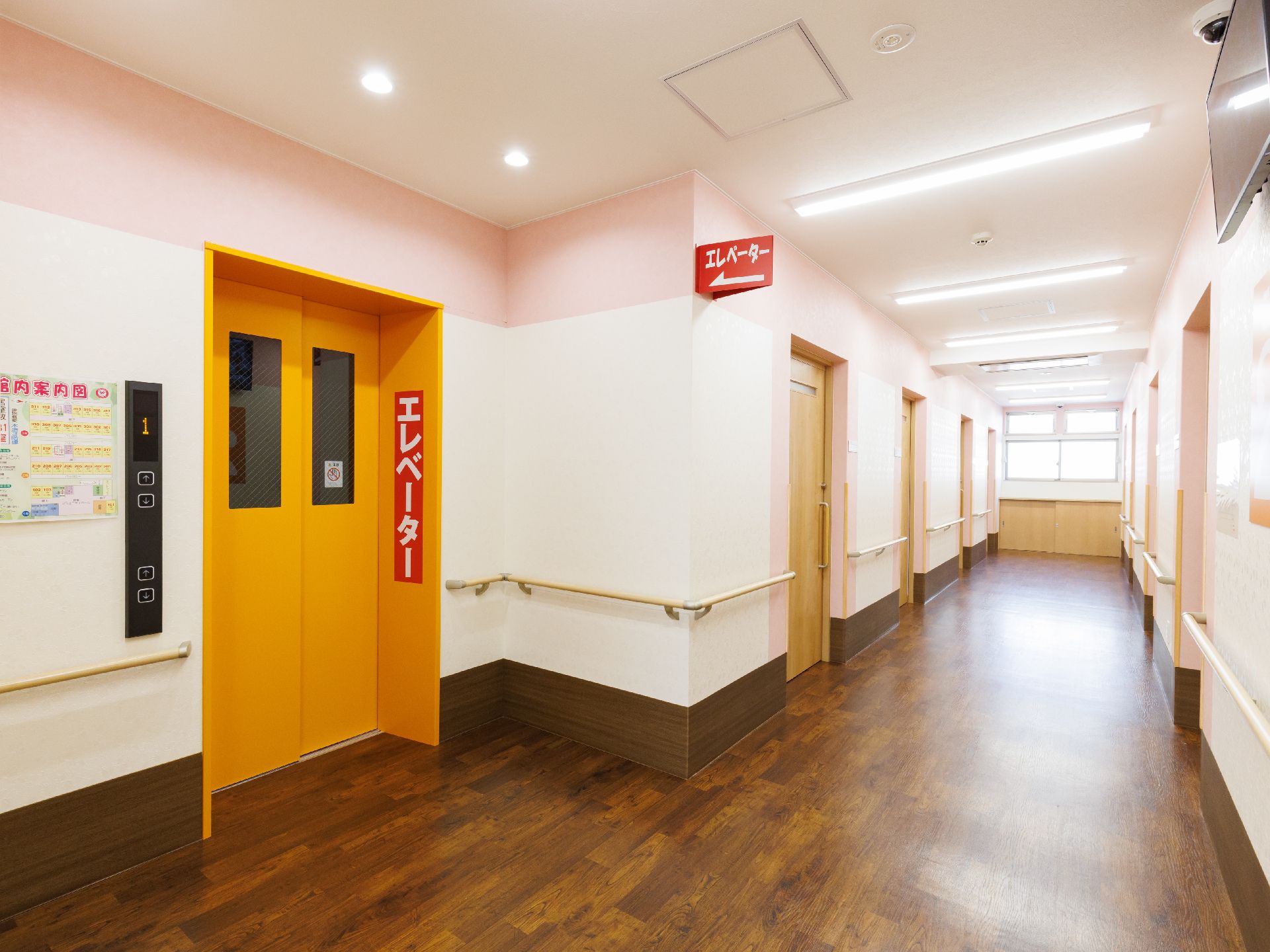 水の入ったコップを持ったエプロンを付けた若い女性スタッフが薬を飲もうとしている高齢女性のそばでほほ笑んでいる。