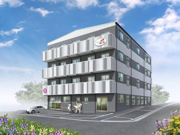 3階建ての建物は白とグレーで各フロアにベランダがあり、玄関には手すり付きのスロープが設置されている。
