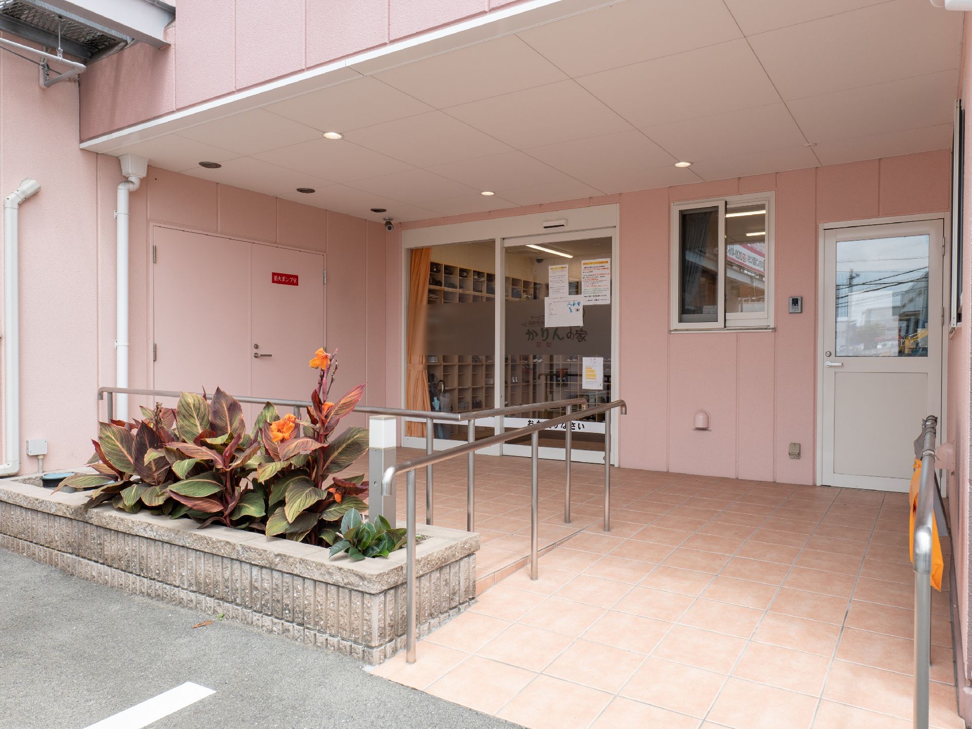 車いすの高齢女性と手を取り合って笑っているピンクのエプロンを付けた若い女性スタッフ。