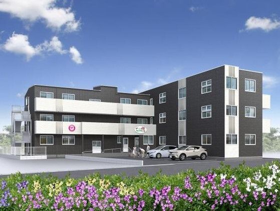 広い駐車場が付いた３階建ての建物。白とダークグレーでエル字型。駐車場には車が２台止まっている。