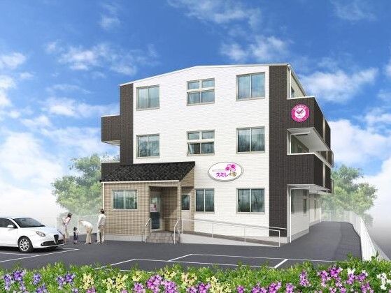 白とダークグレーの３階建ての建物。外壁には住宅名が書かれ、敷地内には駐車場があり、家族連れと高齢者が話している。