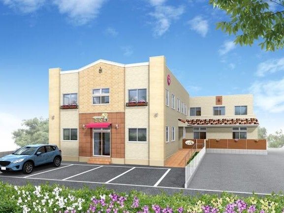 駐車場が付いた２階建ての建物。建物の周辺にはフェンスがあり、草花も植えられている。