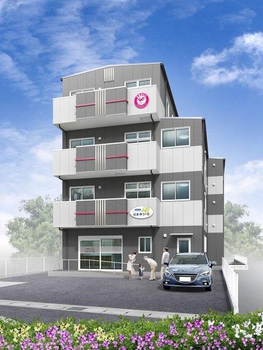 敷地内には駐車場があり、３階建ての建物はダークグレーを基調としていて、外壁には住宅名も書かれている。