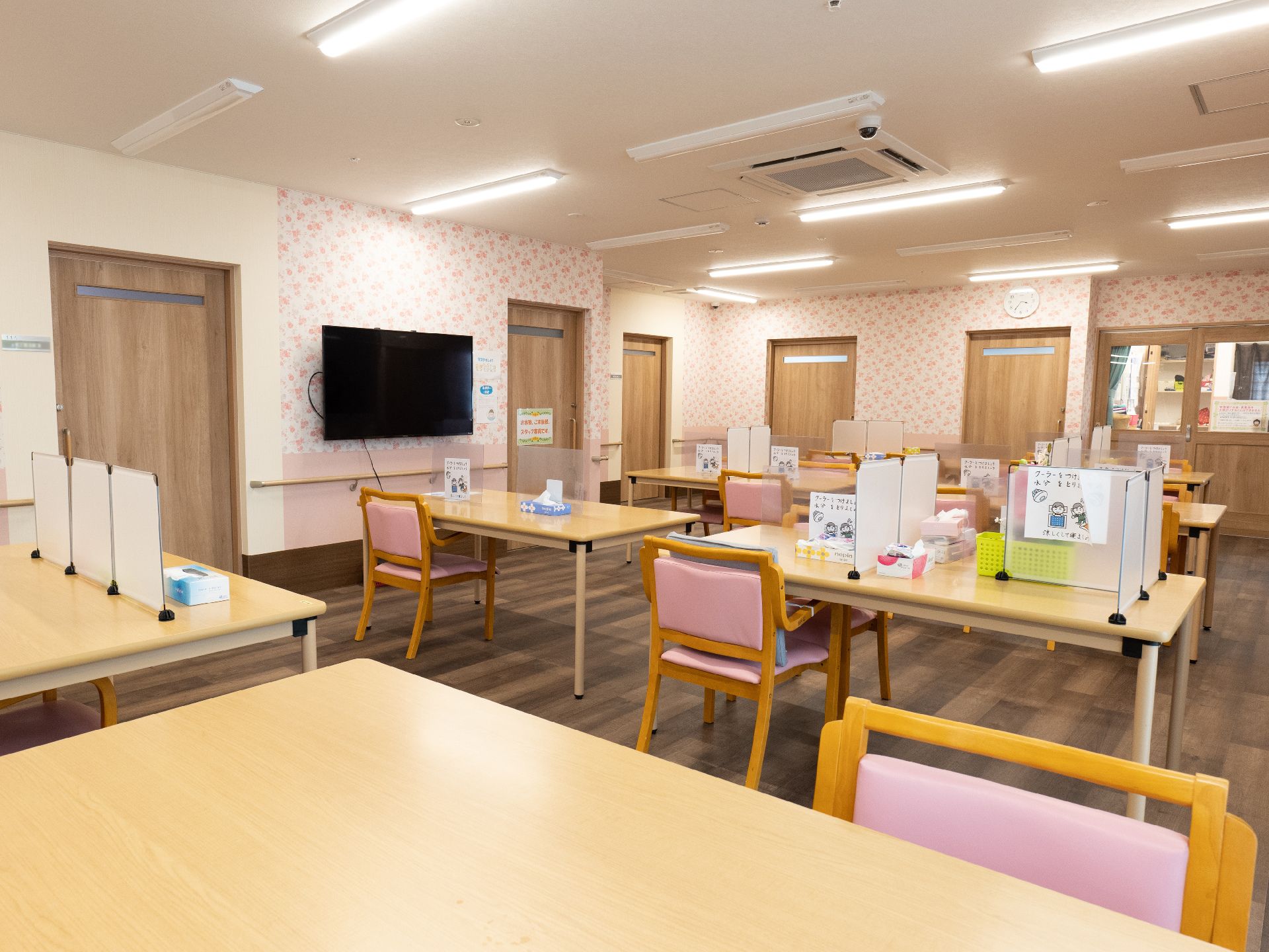 木製の机と椅子が並んでいる白い壁の広間