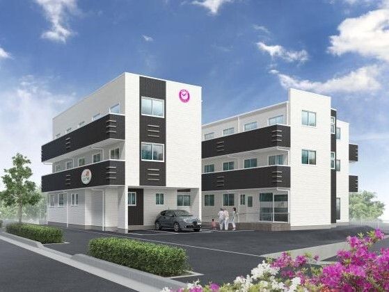 白とダークグレーの３階建ての建物。各フロアにベランダがあり、駐車場が完備されている。