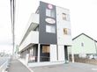 白とダークグレーの3階ての建物。敷地内には駐車場がある。