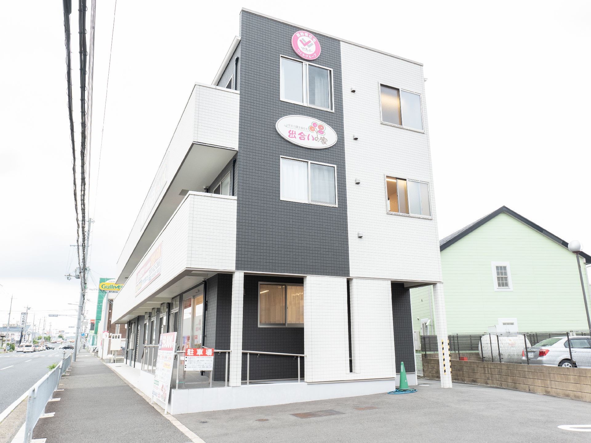 白とダークグレーの３階建ての建物。各フロアにベランダがある。