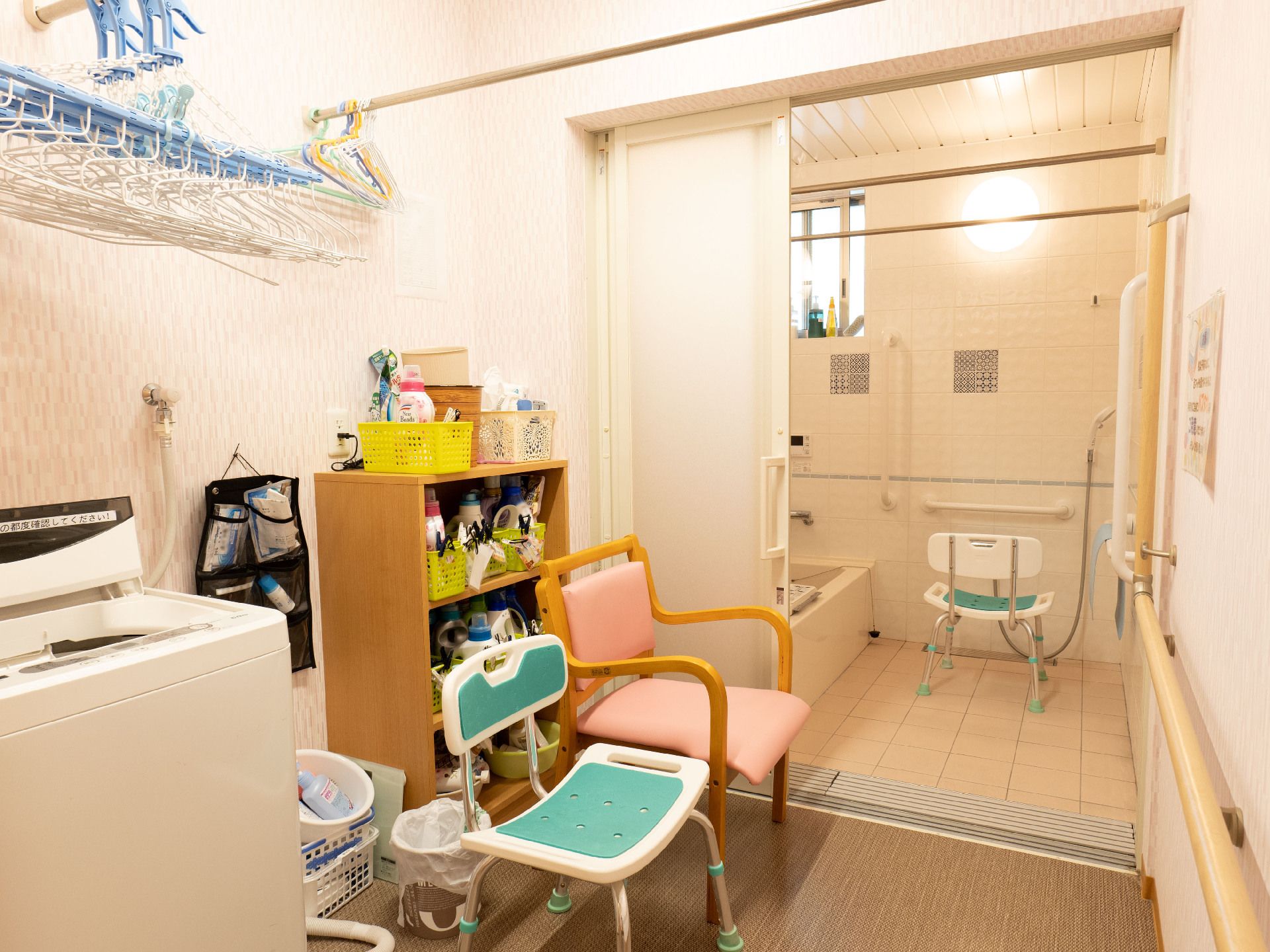 浴室の手前の棚と洗濯機と椅子が壁際に置かれた白い部屋