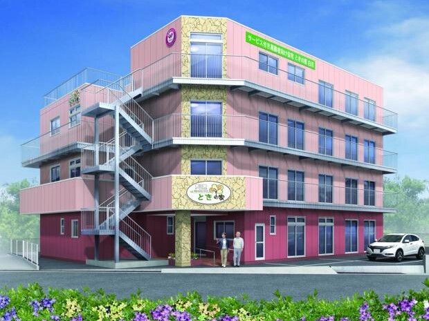 4階建ての建物はピンク系で屋外階段が付き、げんかんのまえには２名の人が立っている。