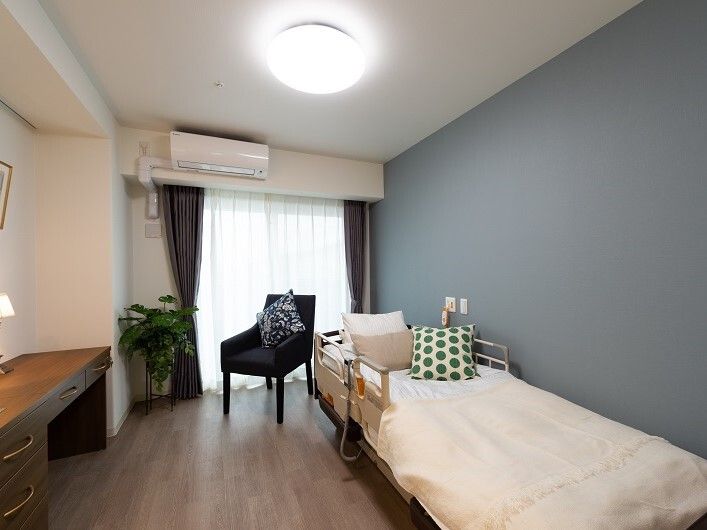 フローリングの部屋には寝具付きのベッドや緊急通報装置、一人用の椅子、デスクなどがある。