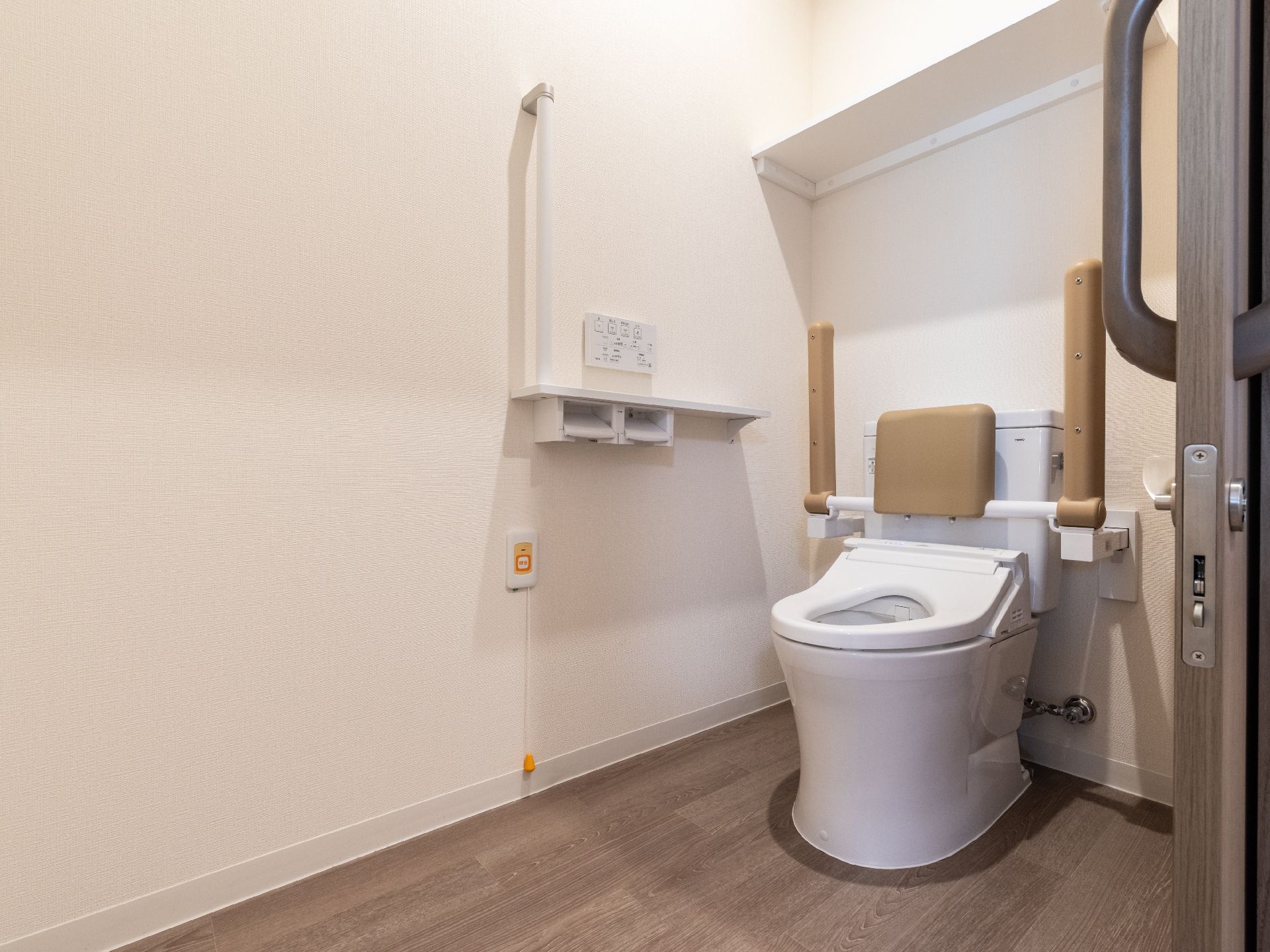 スライド式の扉を開けた先にある木製の手すりが上がった状態でついているトイレが置かれた部屋
