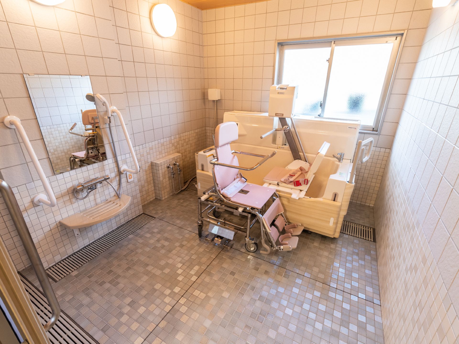 タイル調の部屋に配置された機械浴用の機械とピンクの車いす