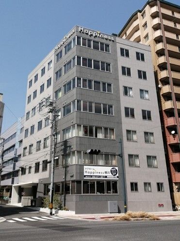 日当たりのいい場所に建っているグレー系の外観の建てに長い建物。道路に面して建っている。