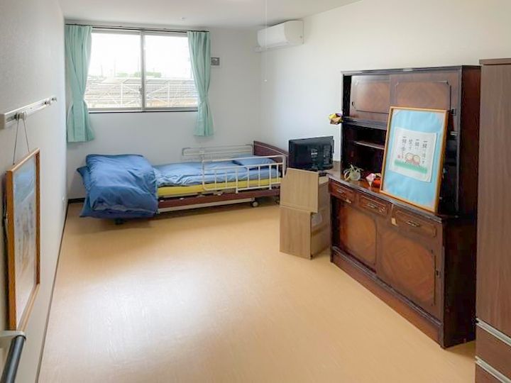 大きなタンスが設置された部屋には寝具付きのベッドがあり、壁にはエアコンや絵画がある。