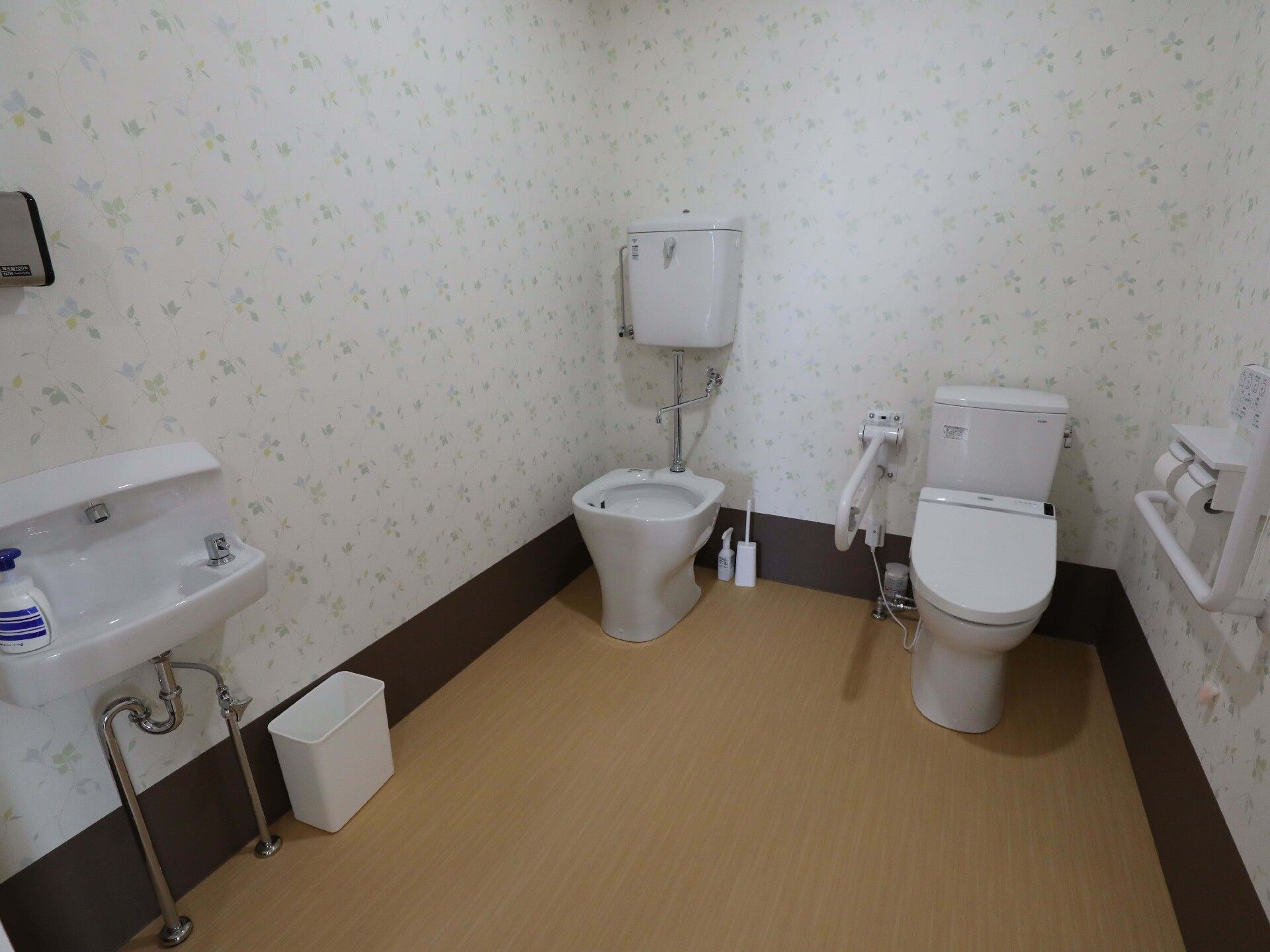 広いトイレ内には手洗い場や洗い場があり、ゴミ箱が置かれ、壁には手すりが付いている。
