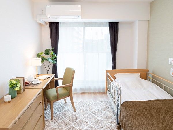 介護用ベッドと広々とした机、1脚の椅子がおいてある個室