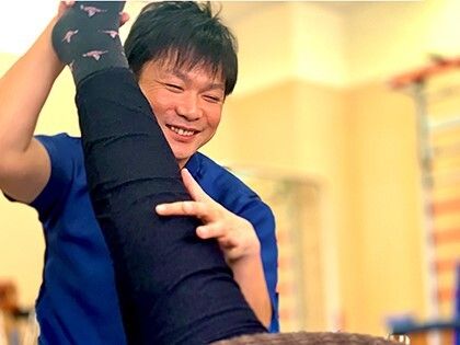 高齢者の方にタオルをかけてマッサージしているスタッフと振り返りながら会話する女性の様子