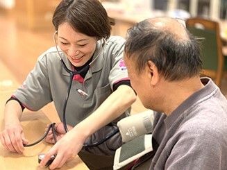 高齢者2名とスタッフが手を握りながら談笑している様子。施設内の会話の一画面